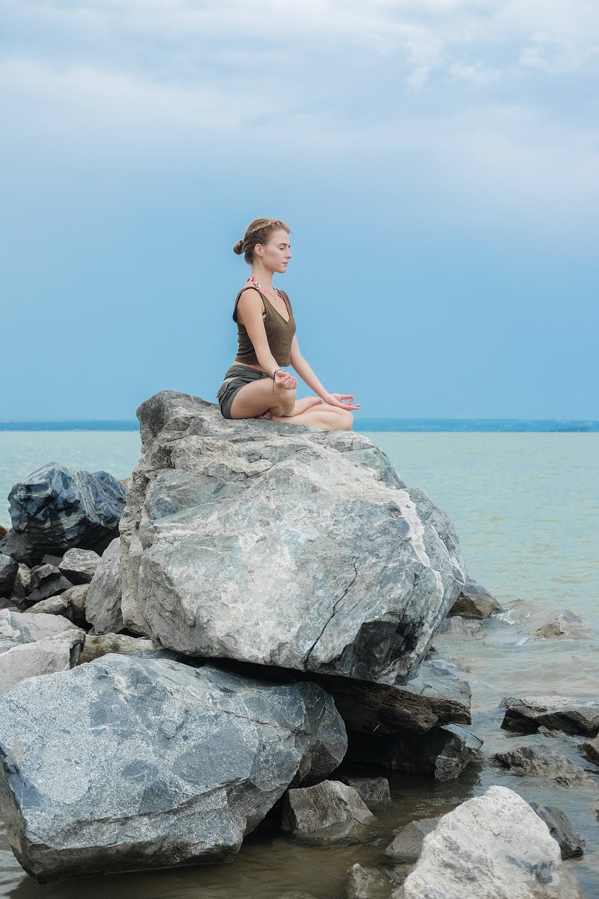 concentrated yoga teacher meditating on large stone